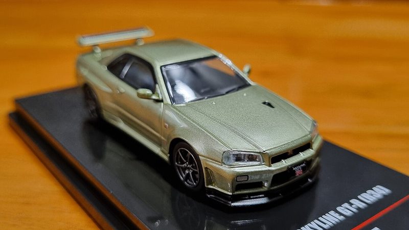 Source photo: a champagne Nissan Skyline diecast model car on a black display base